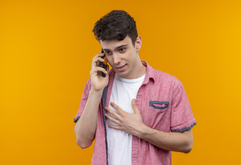 looking at side caucasian young guy wearing pink shirt speaks on phone on isolated orange background